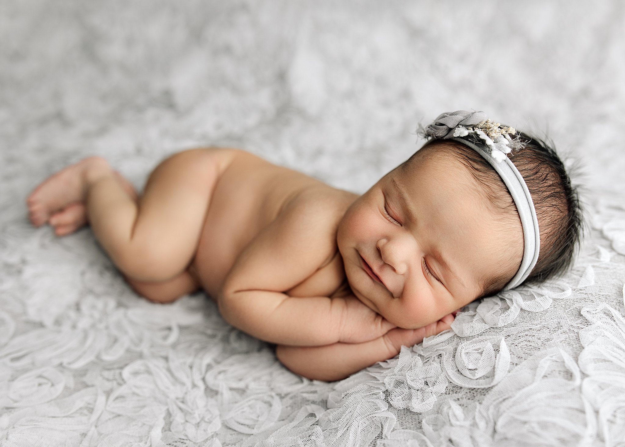 Newborn girl posed on gray fabric smiling